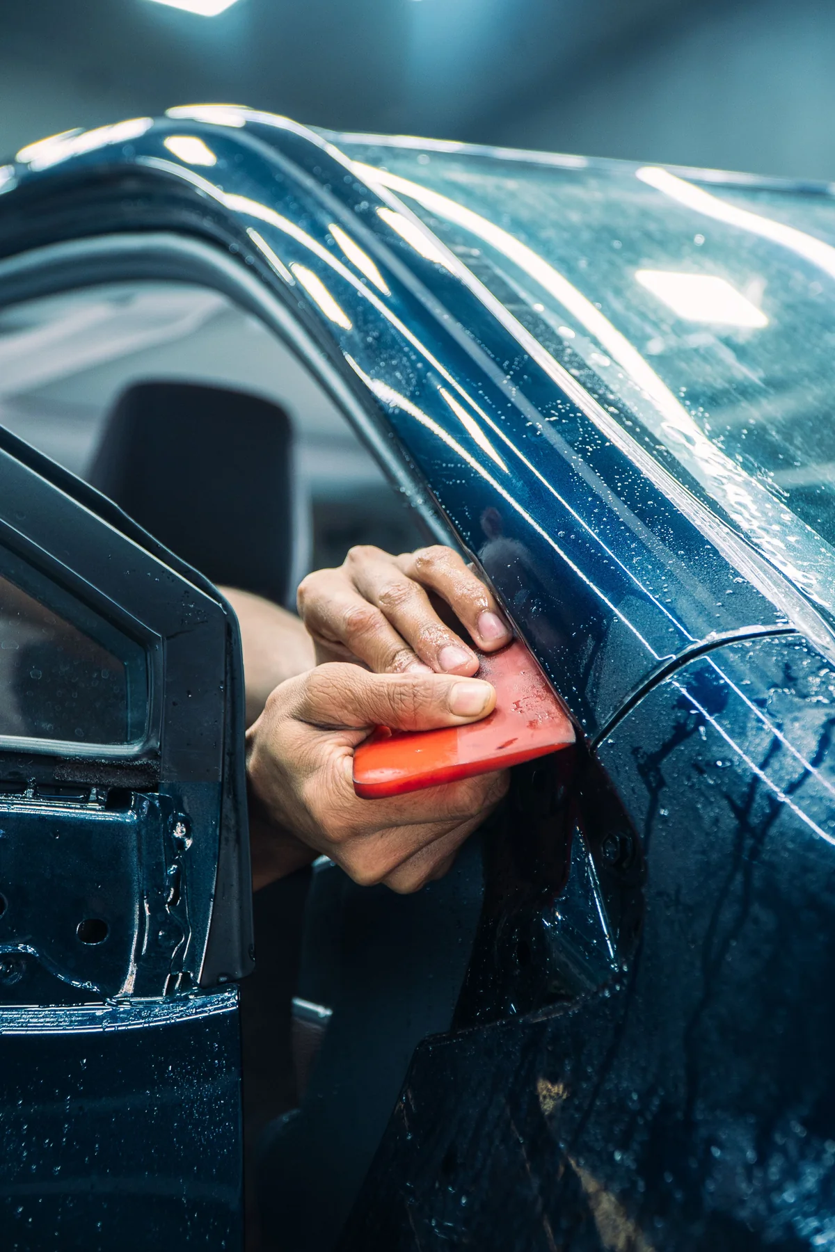 Monteur strijkt transparante lakbeschermingsfolie op een autodeur glad