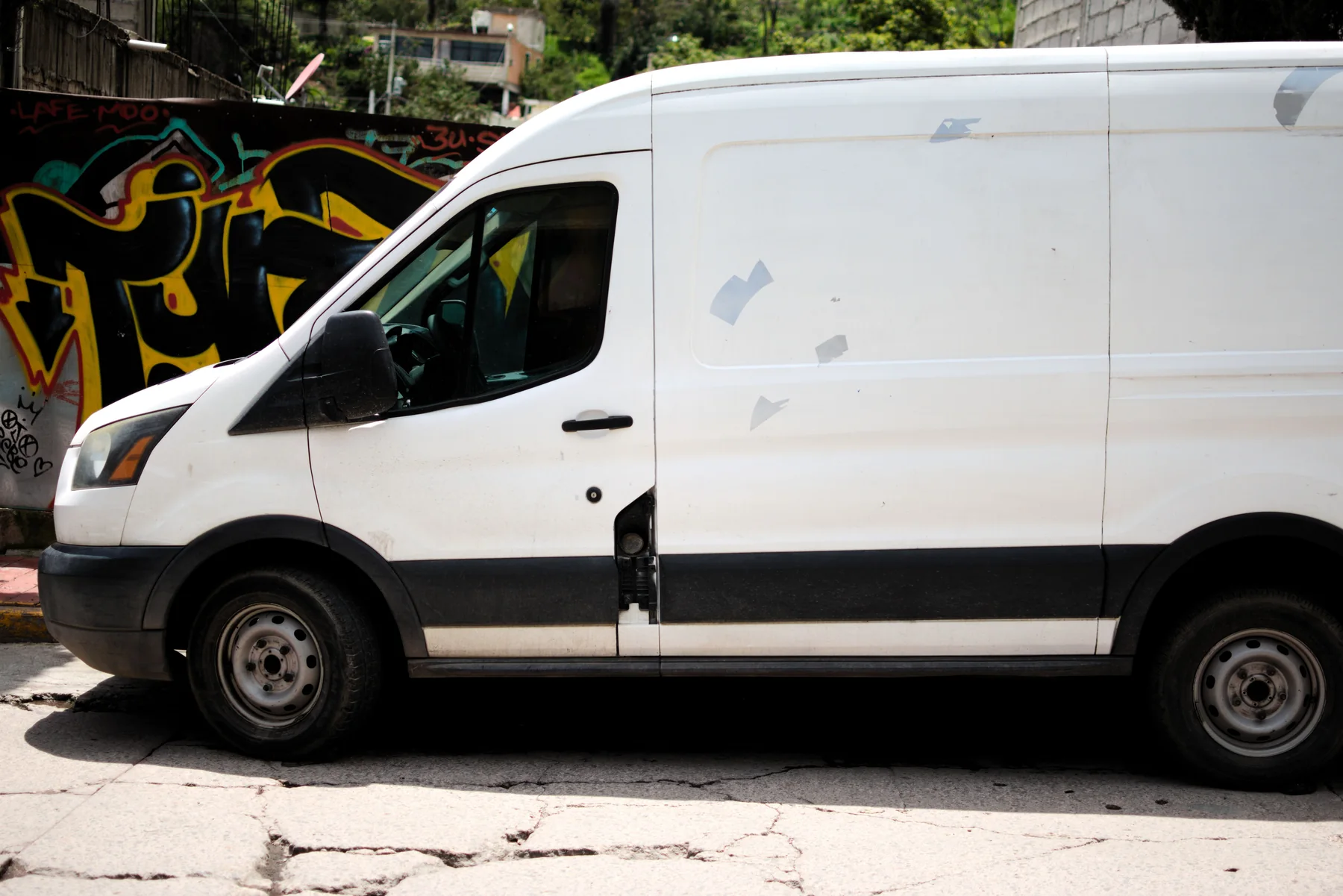 Witte bestelwagen met groot zijpaneel langs een muur